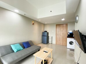 Uma sala moderna com um sofá cinzento, uma mesa de centro de madeira, uma máquina de lavar e uma televisão.