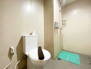 Ein Badezimmer mit Toilette, Dusche und einer grünen Matte am Boden.