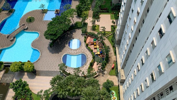 A high-rise hotel with a rooftop pool area featuring multiple swimming pools and a children's play area. - Nice Designed And Elegant 2Br At Green Bay Pluit Apartment (Jakarta)