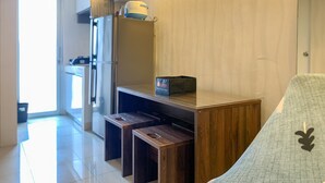 A modern kitchen with a built-in oven, a microwave, and a coffee maker on the countertop. There are two wooden stools and a small table with a box on it. - Nice Designed And Elegant 2Br At Green Bay Pluit Apartment (Jakarta)