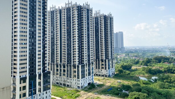 Un immeuble résidentiel de grande hauteur, doté de nombreux étages et de balcons, entouré de verdure et bordé par une rivière.