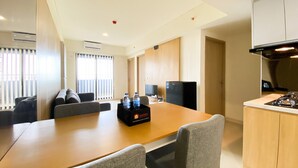 Une chambre d’hôtel moderne dotée d’un coin repas, d’une kitchenette et d’une grande fenêtre avec stores.