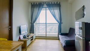 A living room with a wooden desk, a sofa, a television, and a balcony with a railing. - Cozy Stay 1Br At M-Town Signature Apartment (Gading Serpong)