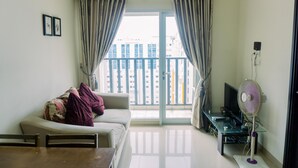 A living room with a sofa, a table, a TV, and a fan. - Fancy And Nice 1Br At Paramount Skyline Apartment (Gading Serpong)