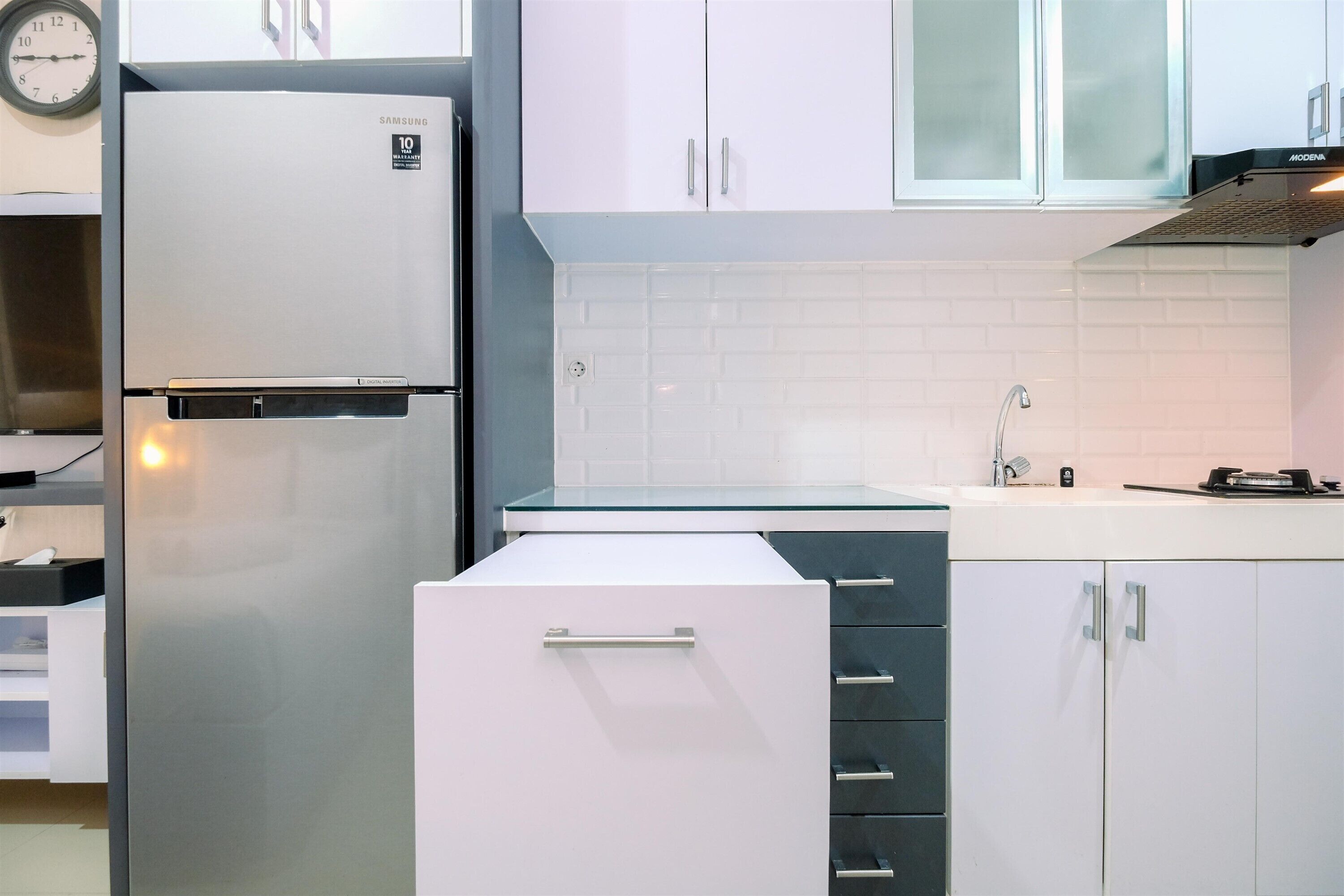 A modern kitchen with white cabinets, a stainless steel refrigerator, and a built-in oven.