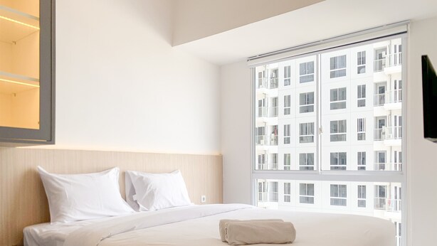 Una habitación de hotel moderna con una cama grande, una mesita de noche y un ventanal con vistas a un edificio.