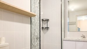 Un baño moderno con ducha de vidrio, estante de madera y espejo que refleja el ambiente.