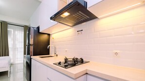 A modern kitchen with white cabinets, a stainless steel refrigerator, a gas stove, and a black range hood. - Minimalist And Best Deal Studio Room At Signature Park Grande Apartment (Jakarta)