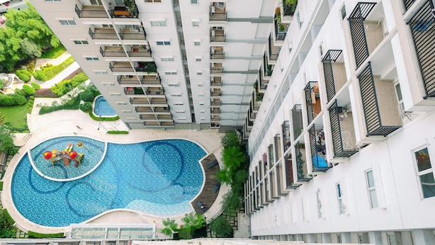 A high-rise building with a central swimming pool, multiple balconies, and surrounding greenery. - Minimalist And Best Deal Studio Room At Signature Park Grande Apartment (Jakarta)