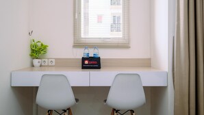 A hotel room with a desk, two chairs, a potted plant, a travel bag, and a window with blinds. - Minimalist And Best Deal Studio Room At Signature Park Grande Apartment (Jakarta)