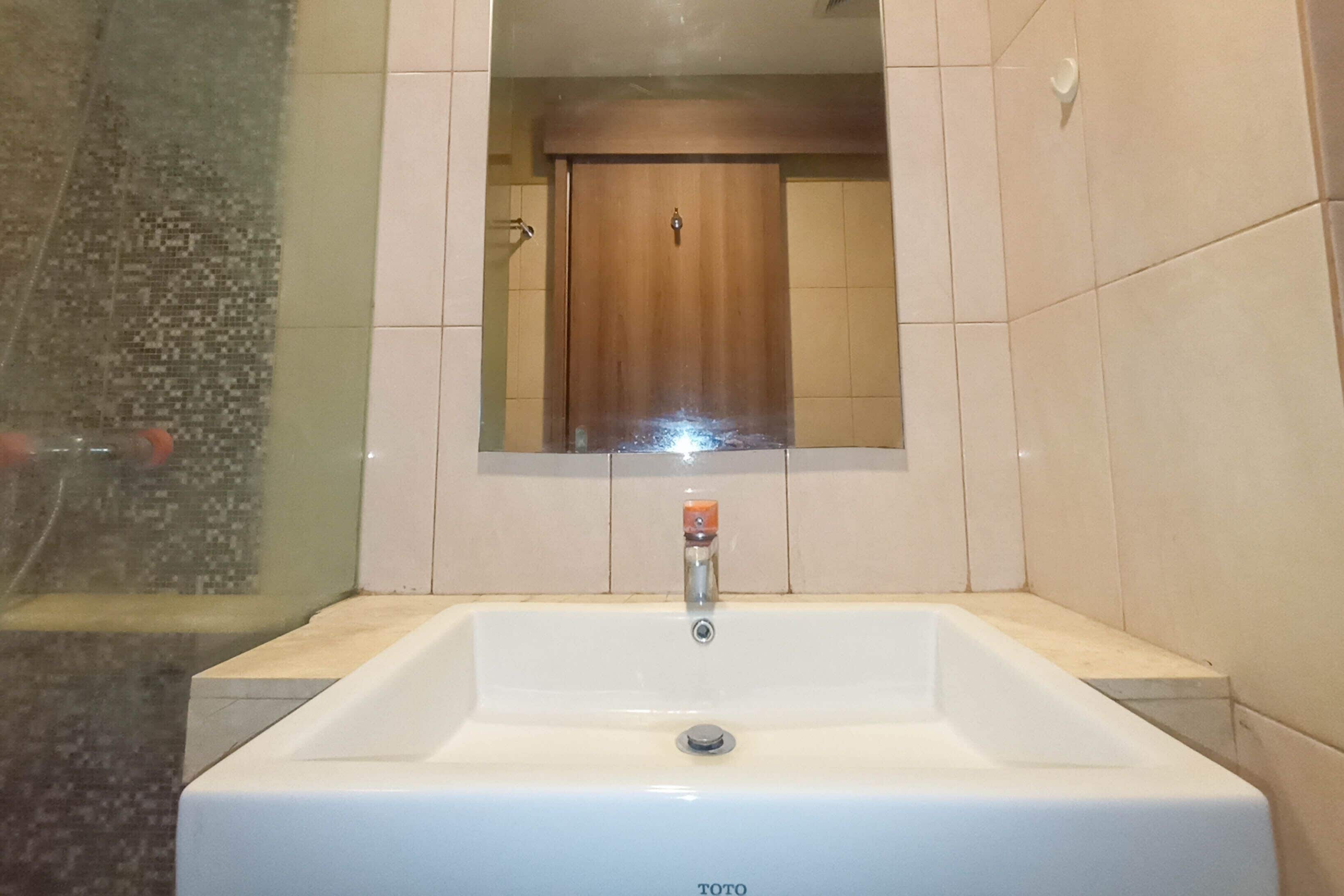 Une salle de bain avec un lavabo blanc, un miroir au-dessus et une porte en bois à l’arrière-plan.
