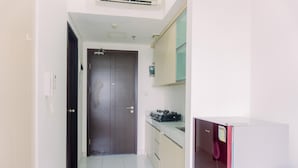 A narrow hallway leading to a closed door with a small kitchen area on the right, featuring cabinets and a countertop. - Good Deal And Warm Studio Room Casa De Parco Apartment (South Tangerang)