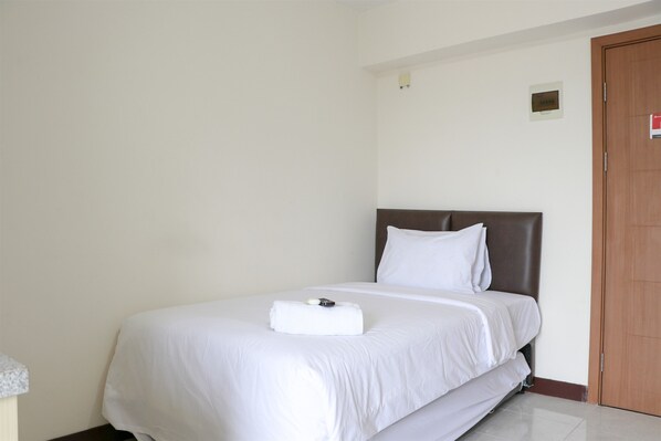 Uma cama bem arrumada com roupa de cama branca, cabeceira marrom e uma pequena mesa de cabeceira com abajur.