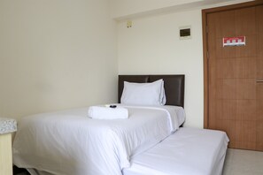 A hotel room with a single bed, a wooden door, and a small wall-mounted light. - Simple And Enjoy Living Studio Room At Cinere Resort Apartment (Depok)