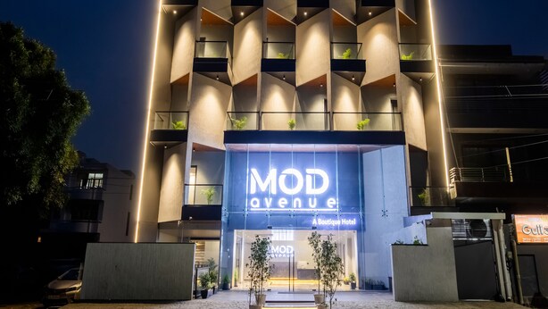 Un hotel moderno con un llamativo letrero 'MOD Avenue', que presenta una fachada geométrica con balcones y una entrada acogedora.
