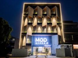 Un hotel moderno con un llamativo letrero 'MOD Avenue', que presenta una fachada geométrica con balcones y una entrada acogedora.