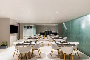 A modern conference room with white chairs, black tables, and a flat-screen TV on the wall.