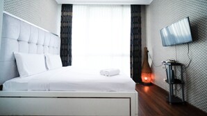 Une chambre d’hôtel moderne dotée d’un grand lit, d’un téléviseur à écran plat fixé au mur et d’une table de chevet avec une lampe.
