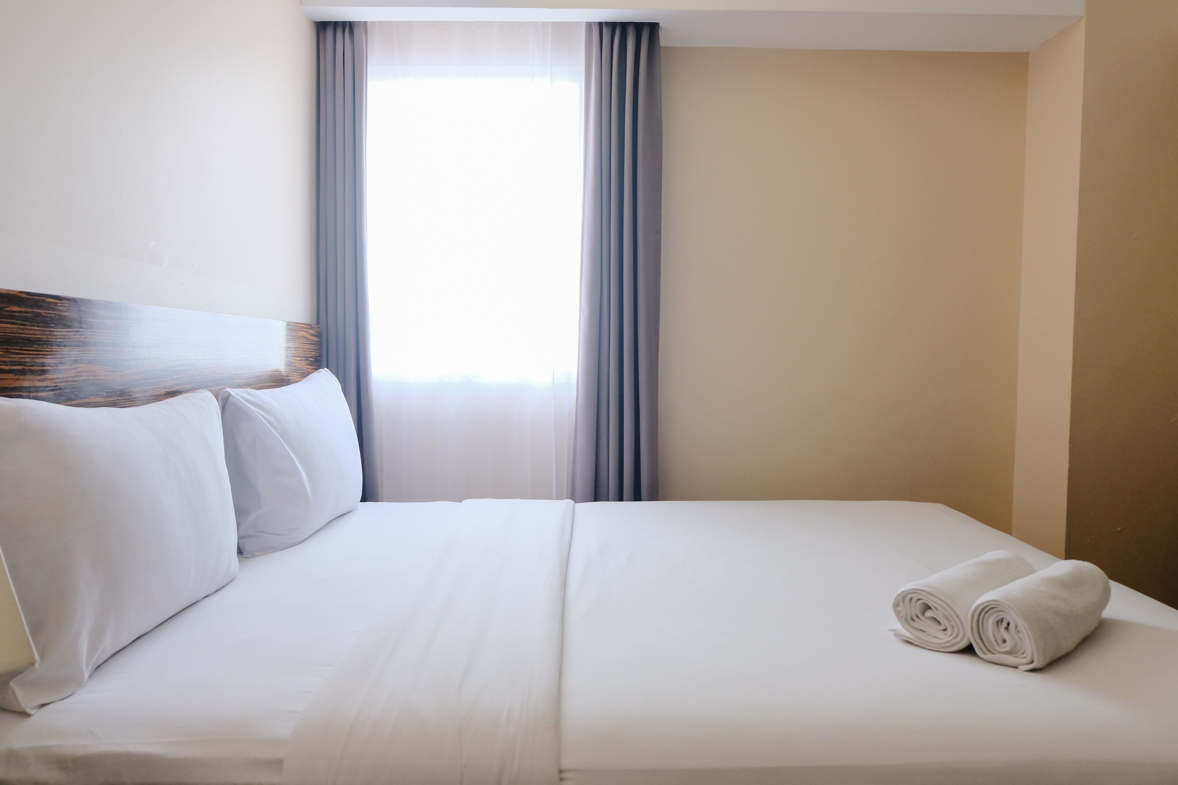 A neatly made bed with white linens, a headboard, and two rolled towels on the side.