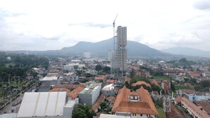 A cityscape with a prominent high-rise building under construction, surrounded by residential buildings and greenery. - Minimalist Studio at Harvard Jatinangor Apartment (Cileunyi)