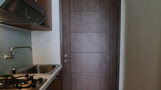 A kitchen with a gas stove, stainless steel sink, and wooden cabinets. - Minimalist Studio at Harvard Jatinangor Apartment (Cileunyi)