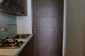 A kitchen with a gas stove, stainless steel sink, and wooden cabinets. - Minimalist Studio at Harvard Jatinangor Apartment (Cileunyi)