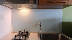 A kitchen with a gas stove, a stainless steel sink, and wooden cabinets. - Best Deal Studio at Harvard Jatinangor Apartment (Cileunyi)