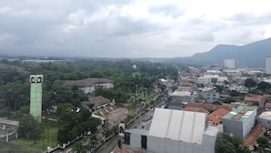 A cityscape with a prominent green tower, dense urban buildings, and a mountain in the background. - Best Deal Studio at Harvard Jatinangor Apartment (Cileunyi)