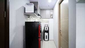 A narrow hallway with a black refrigerator, a water dispenser, and a microwave on a shelf. - Nice And Comfy Studio At Grand Dharmahusada Lagoon Apartment (Surabaya)