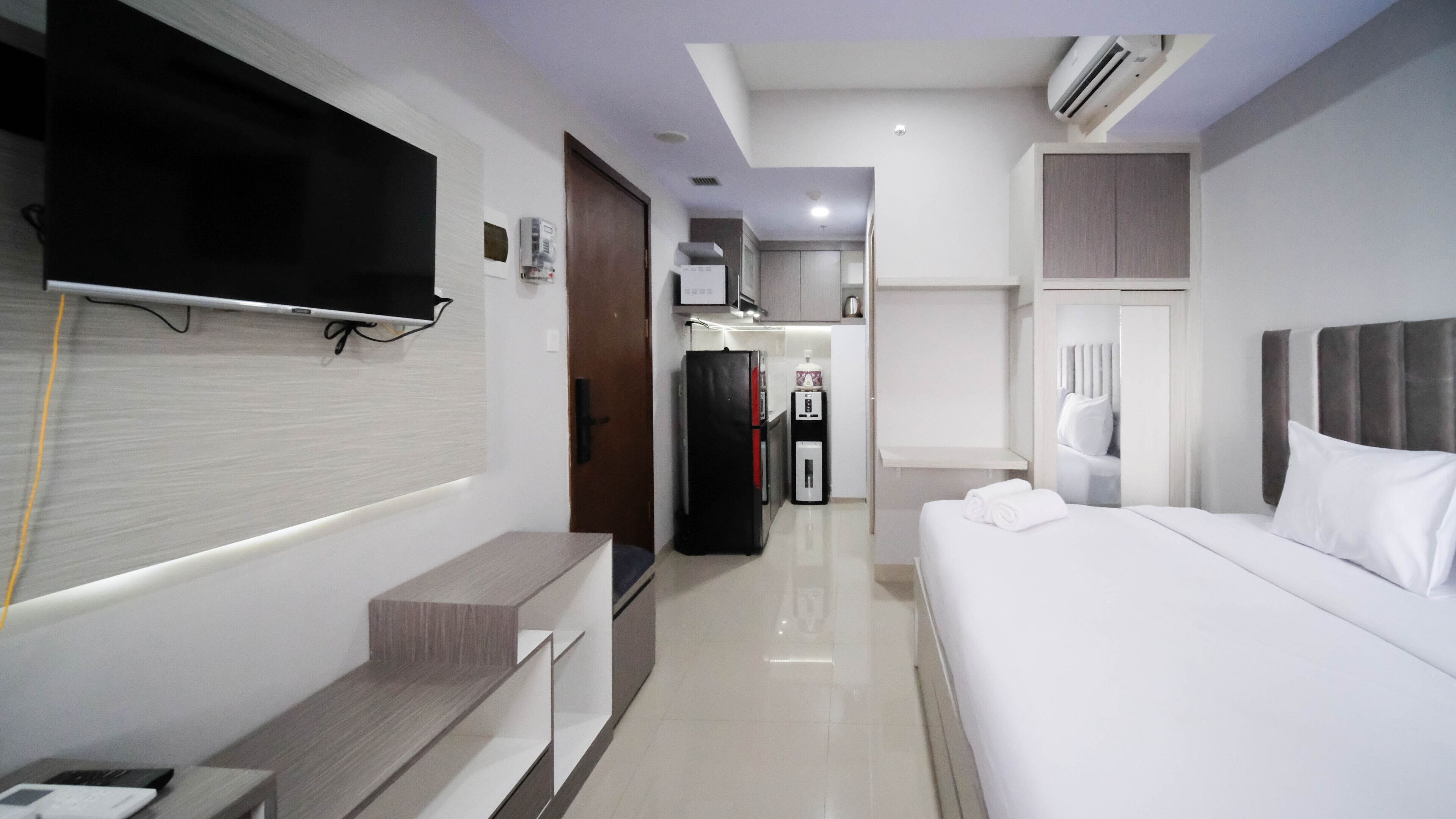 Een hotelkamer met een bed, een aan de muur bevestigde televisie, een klein bureau en een kledingkast.