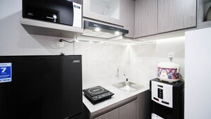 A compact kitchen with a black refrigerator, a sink, a coffee maker, and a microwave. - Nice And Comfy Studio At Grand Dharmahusada Lagoon Apartment (Surabaya)