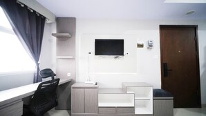 A modern room with a TV mounted on the wall, a desk with a chair, and a door. - Nice And Comfy Studio At Grand Dharmahusada Lagoon Apartment (Surabaya)