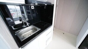 Uma cozinha compacta com bancada preta, pia de aço inoxidável e coifa embutida.