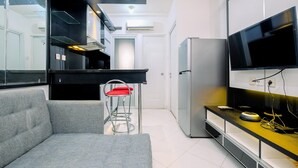 A modern kitchen with a grey sofa, a red chair, a TV, and a refrigerator. - Best Deal And Modern 1Br Green Pramuka City Apartment (Jakarta)