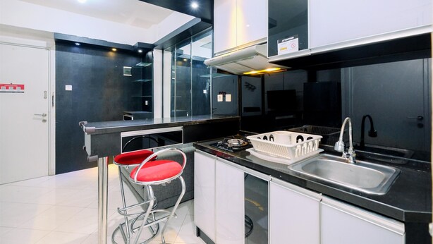 A modern kitchen with a black countertop, stainless steel sink, and a red bar stool. - Best Deal And Modern 1Br Green Pramuka City Apartment (Jakarta)