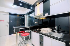 A modern kitchen with a black countertop, stainless steel sink, and a red bar stool. - Best Deal And Modern 1Br Green Pramuka City Apartment (Jakarta)