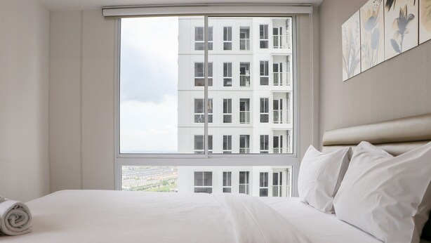 Quarto de hotel com uma janela grande, uma cama bem arrumada e vista para um edifício.