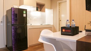 Uma cozinha compacta com geladeira preta, bancada branca e minibar com água engarrafada.