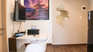 Quarto de hotel com escrivaninha, TV de tela plana na parede, pintura de um pagode e um detalhe hexagonal decorativo na parede.