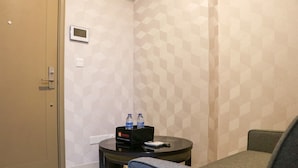 A hotel room with a bed, a small table with a remote control, a chair, and a minibar with bottled water. - Nice And Relaxing 1Br At Gold Coast Apartment (Jakarta)