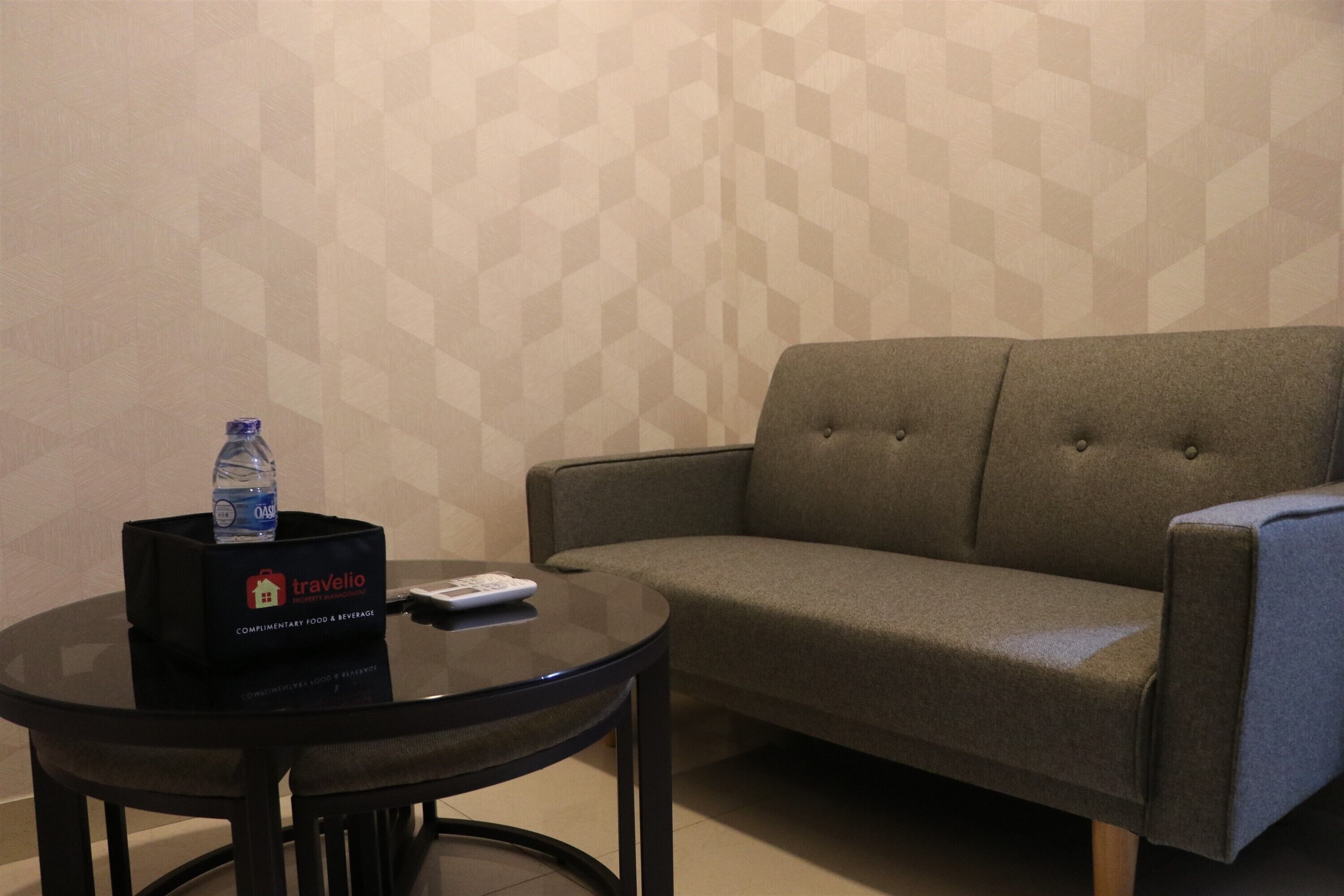 Una habitación con un sofá gris, una mesita redonda con una botella de agua y una bandeja, y una pared con un diseño geométrico.