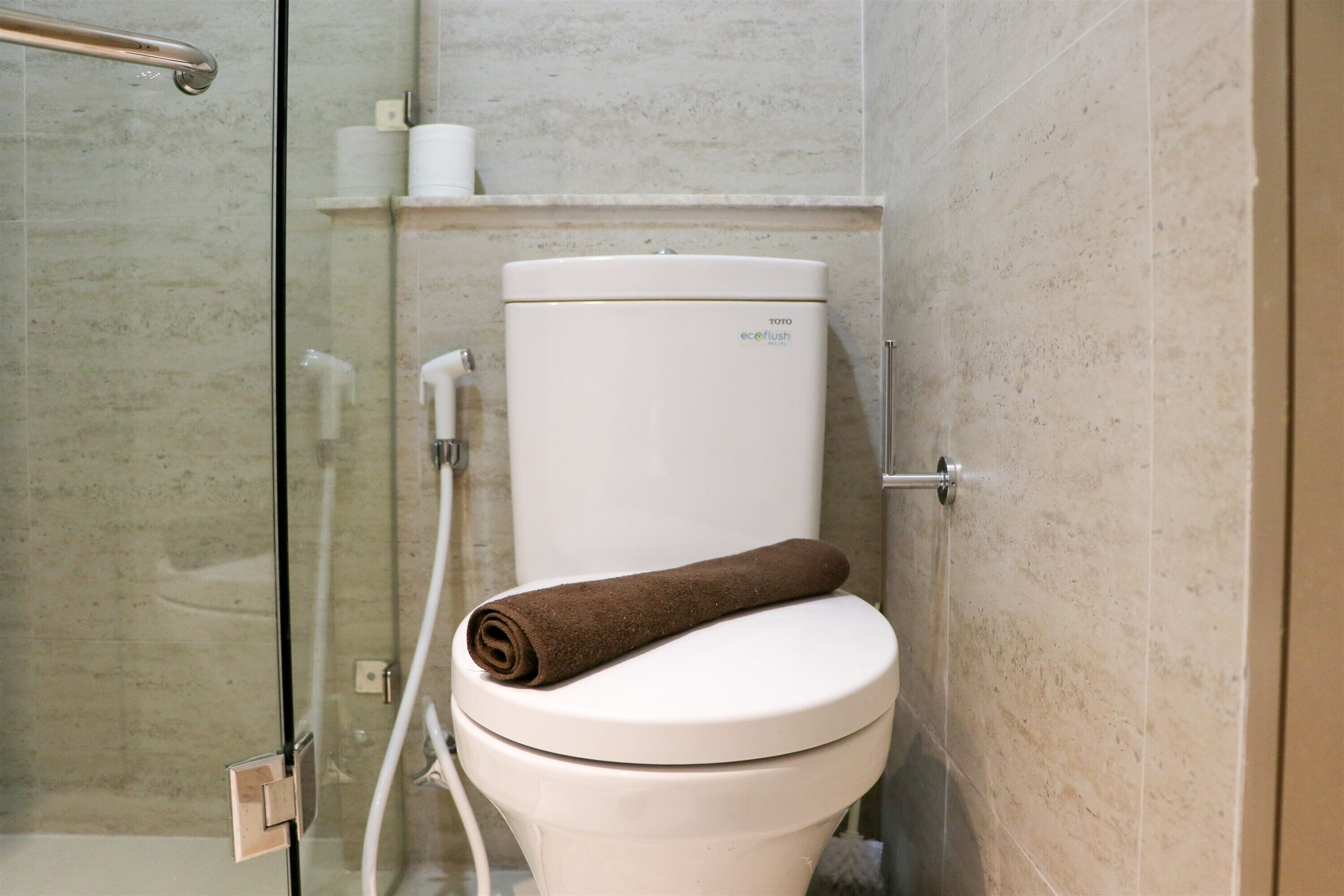 A bathroom with a white toilet, a glass shower enclosure, and a towel on the toilet seat.