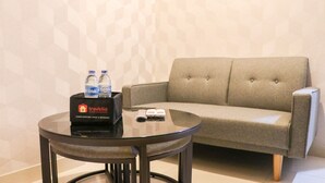 A room with a grey sofa, a glass table with a black tray containing a travel kit, and a patterned wall. - Nice And Relaxing 1Br At Gold Coast Apartment (Jakarta)
