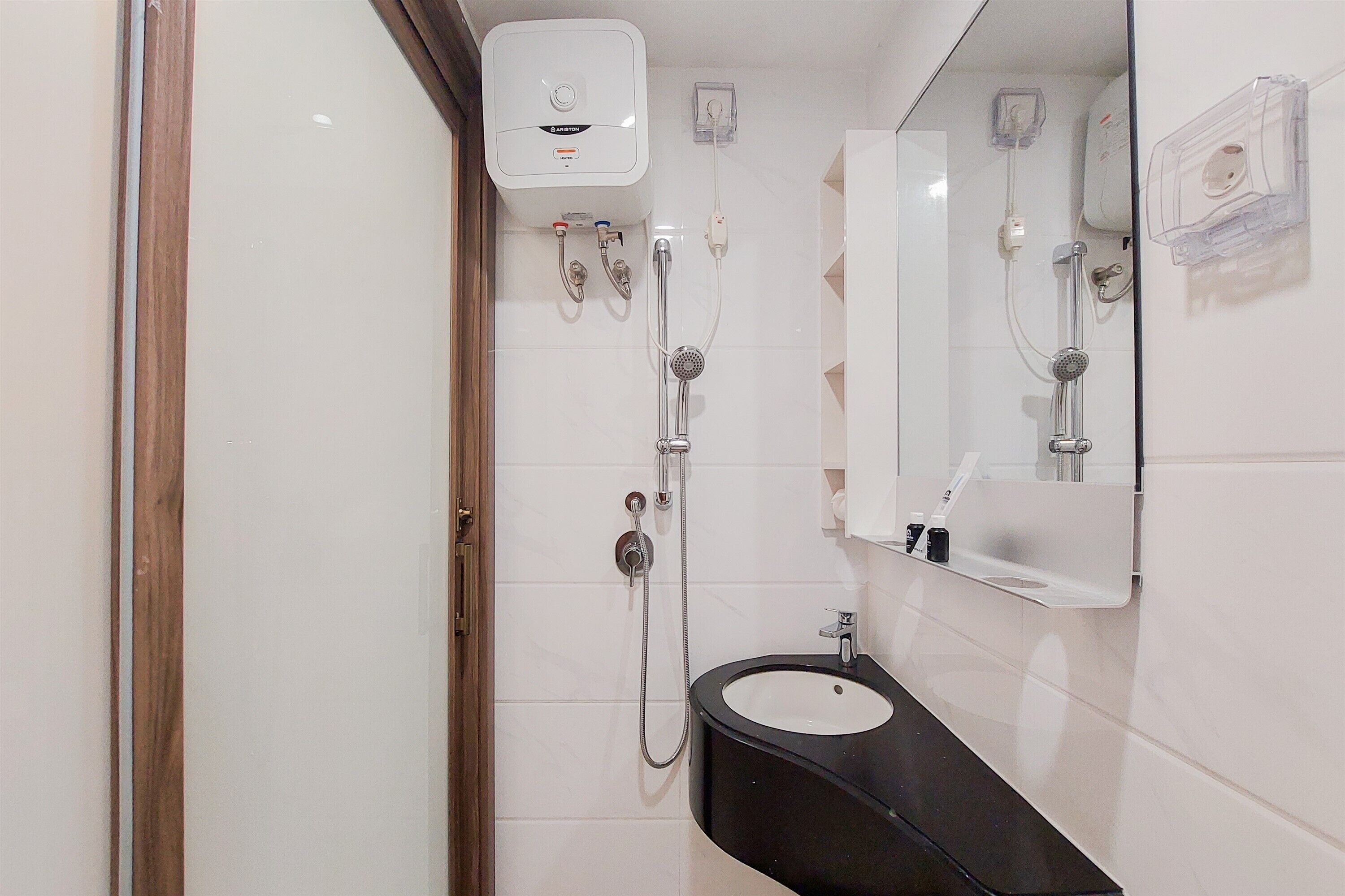 Um banheiro com parede revestida de azulejos brancos, pia preta, espelho e chuveiro com chuveirinho.