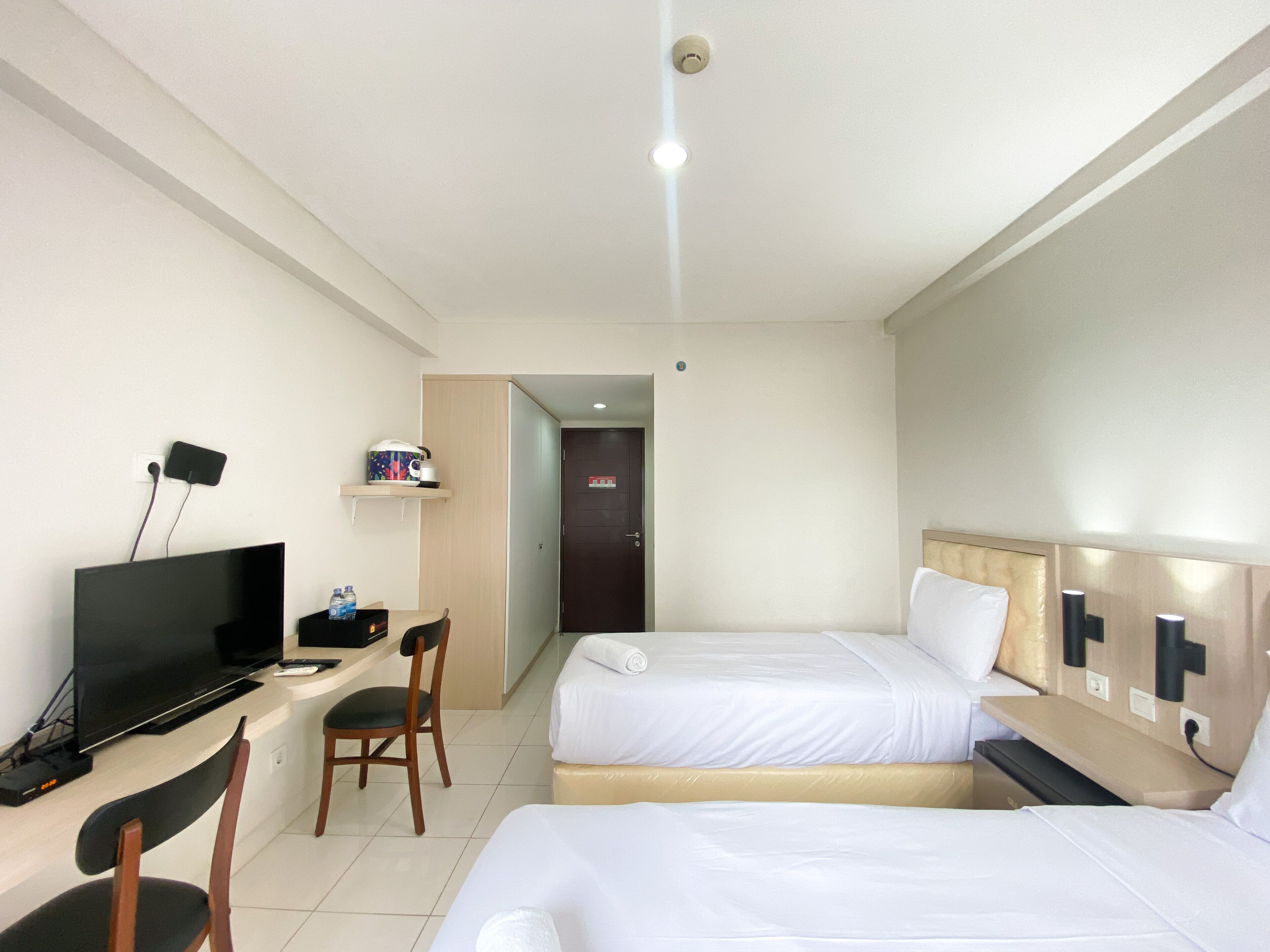 Una habitación de hotel con escritorio, dos camas, televisor y una silla.