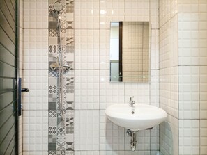 A bathroom with a shower, a sink, and a mirror. - Homey Studio At De Prima Apartment (Medan)