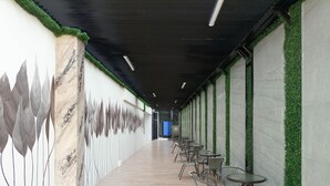 Un pasillo con una larga zona de asientos con banco, un mural en la pared izquierda y detalles de follaje verde en la pared derecha.