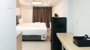 A hotel room with a bed, a desk, a refrigerator, and a curtain.