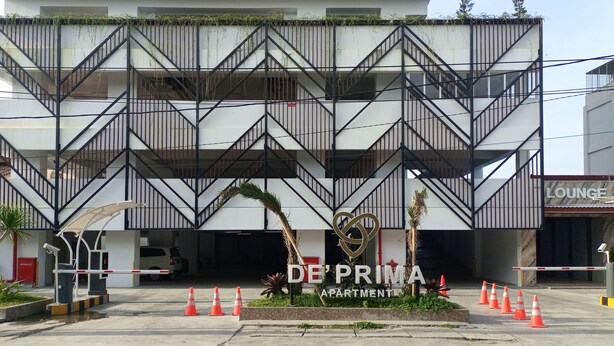 A modern building with a zigzag metal railing, a gated entrance, and a sign for 'DE PRIMA APARTMENTS'.