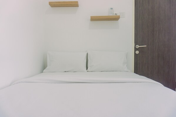 A neatly made bed with white linens, a wooden door, and two wooden shelves above it.